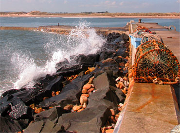 Waves crashing over Beadnell Harbour with Beadnell Bay in the Background